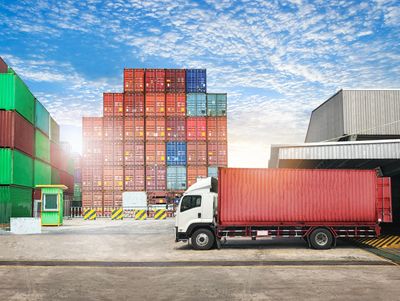 Red semi-truck parked by cargo containers
