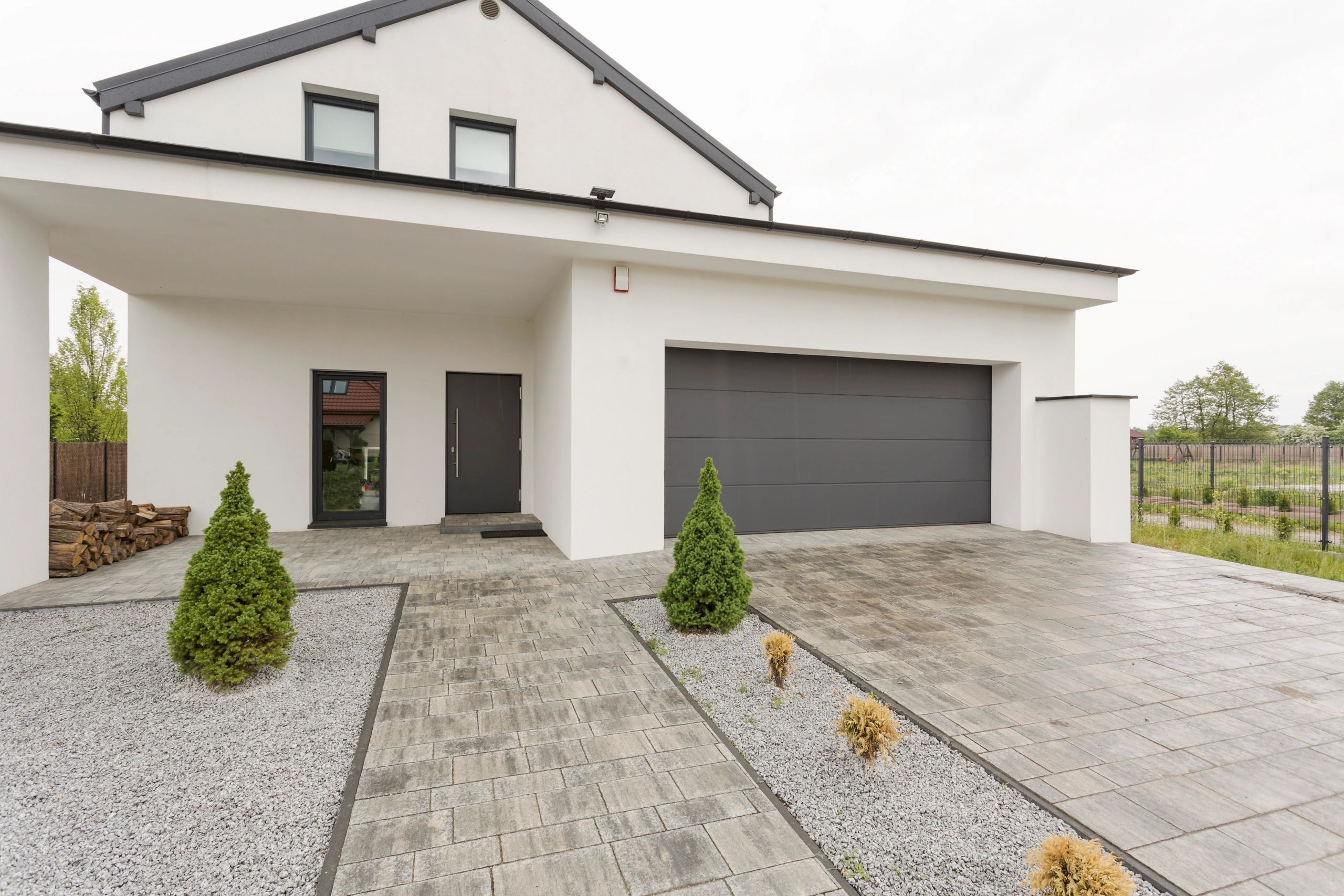 Modern white house with a black garage door and neatly landscaped front yard.