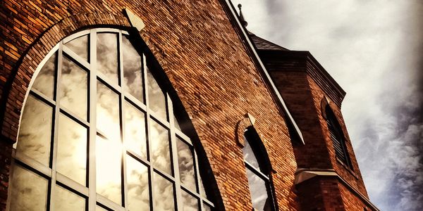 Sunlit brick building with large arched windows reflecting clouds.