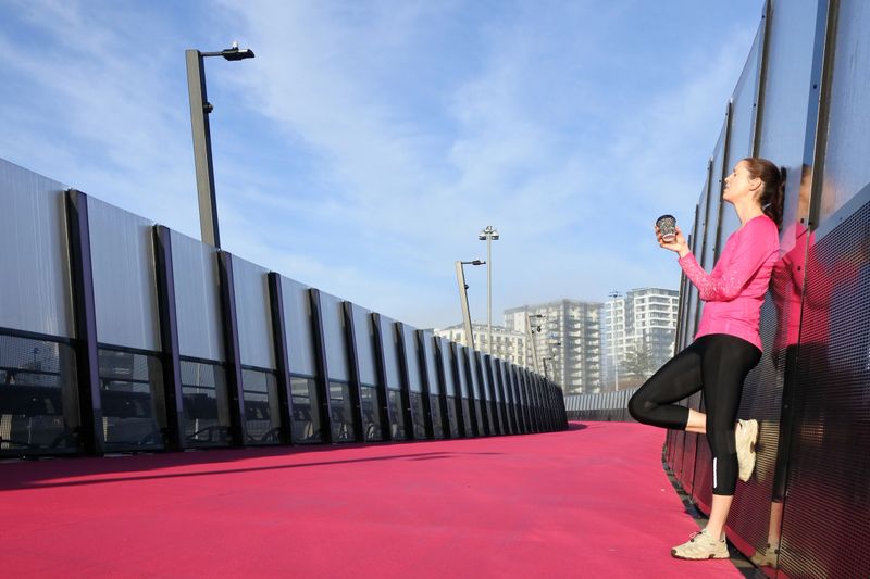 Young woman (age 30) has a coffee break from running on a bright pink cycleway road in Auckland, New Zealand. Real people. Copy space.