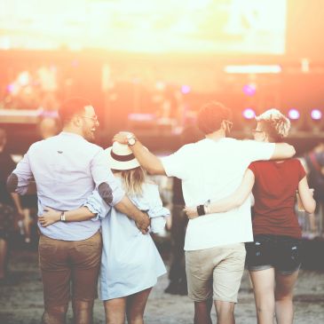 Four friends walking arm-in-arm at an outdoor event with warm lighting.