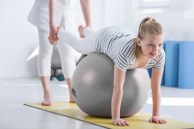 Child balancing on exercise ball with adult support.