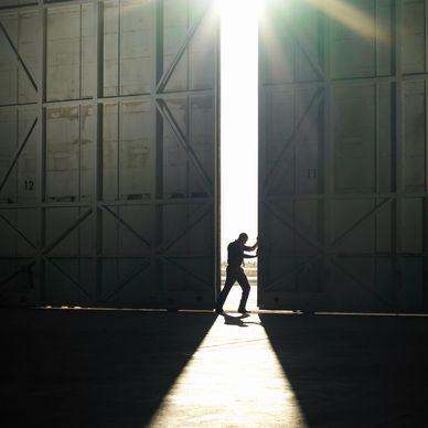 Silhouette of a person pushing open large doors with bright sunlight streaming in.