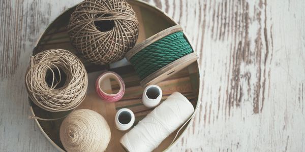 Various colored twine and thread spools in a round tin on a wooden surface.