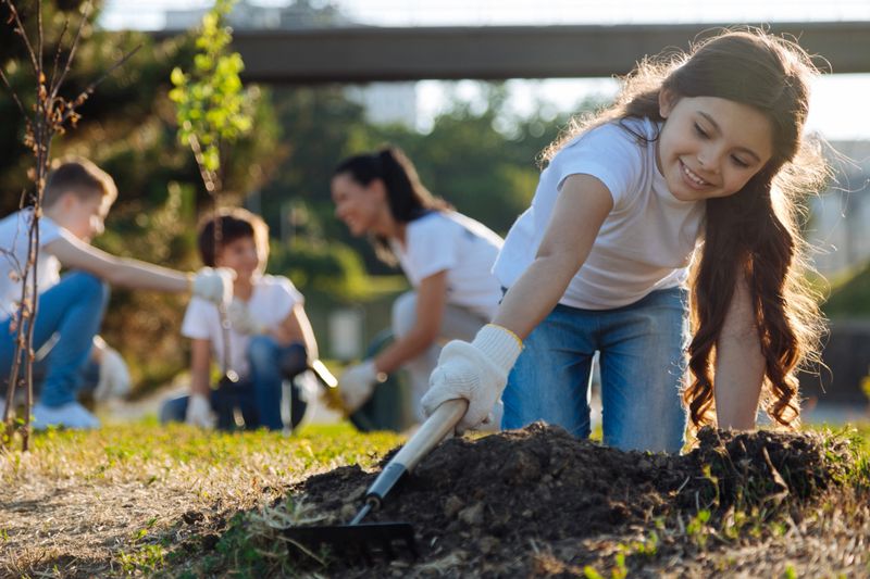 Sunny day. Positive delighted girl bowing her head and keeping smile on face while standing on knees while planting