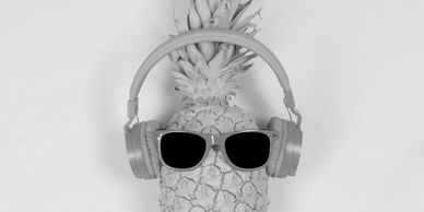 Turquoise pineapple with pink sunglasses and headphones on yellow background.