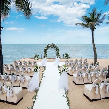 White aisle on sandy beach leads to green arched canopy with ocean backdrop at Dreams Las Mareas.
