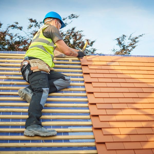 Construction worker installing roof tiles on a sunny day.