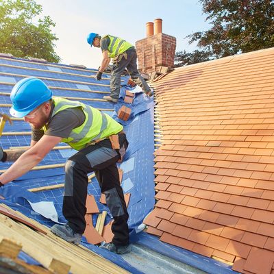 Two construction workers installing roof tiles on a house.