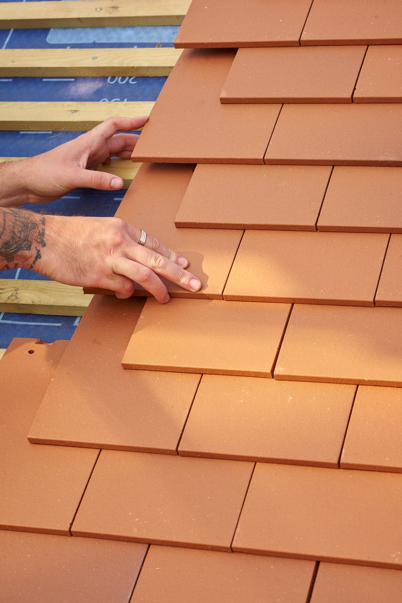 a roofer nails on the roof tiles