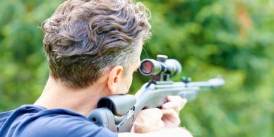 Man aiming with a rifle scope outdoors.