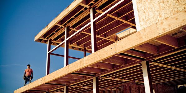 Construction worker stands on the wooden frame of a house under a clear blue sky.