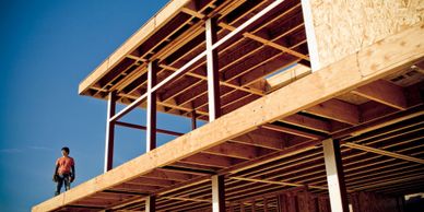Construction worker on a wooden building framework under clear blue sky.
