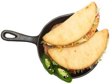 Two tacos served in a small cast iron skillet with sliced jalapeños.