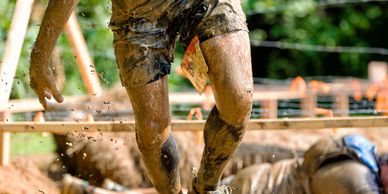 Person running through a muddy obstacle course outdoors.