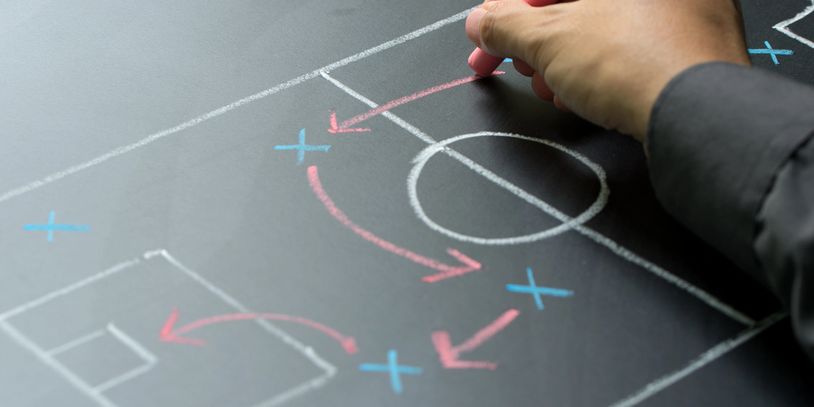 Hand drawing soccer strategy with chalk on a blackboard.