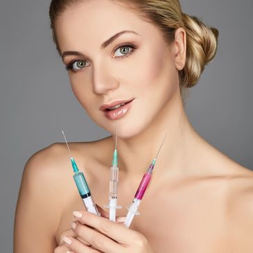 Woman holding three syringes with colorful liquids, posing against a gray background.