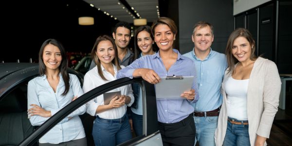 Happy team at a car dealership posing with clipboard.
