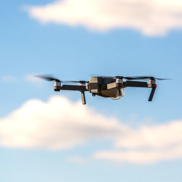A drone flying against a blue sky with scattered clouds.