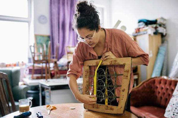 Woman measuring the wooden frame of a chair with springs.