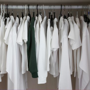Closet rod with mostly white shirts and one green shirt hanging.