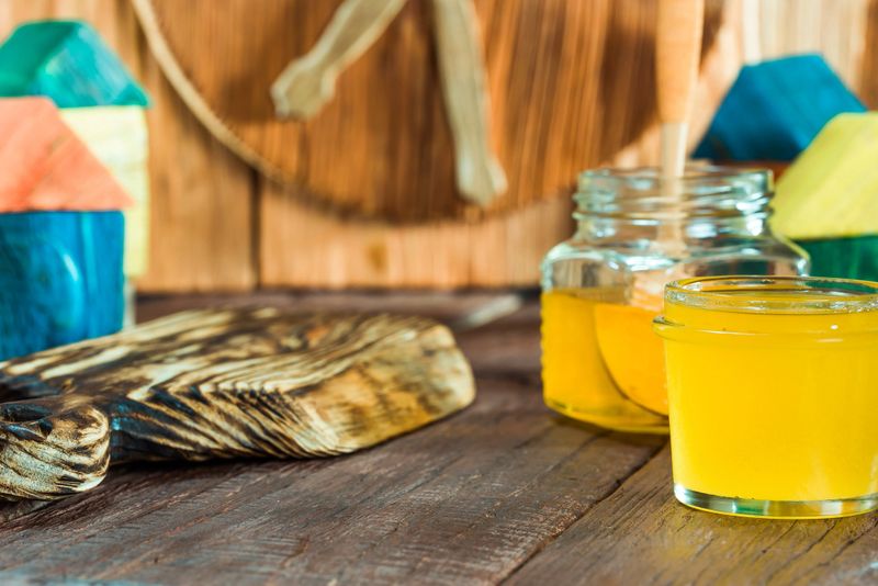 Honey in glass jar standing on wooden table among colorful toy wooden houses looking like beehives. Close-up