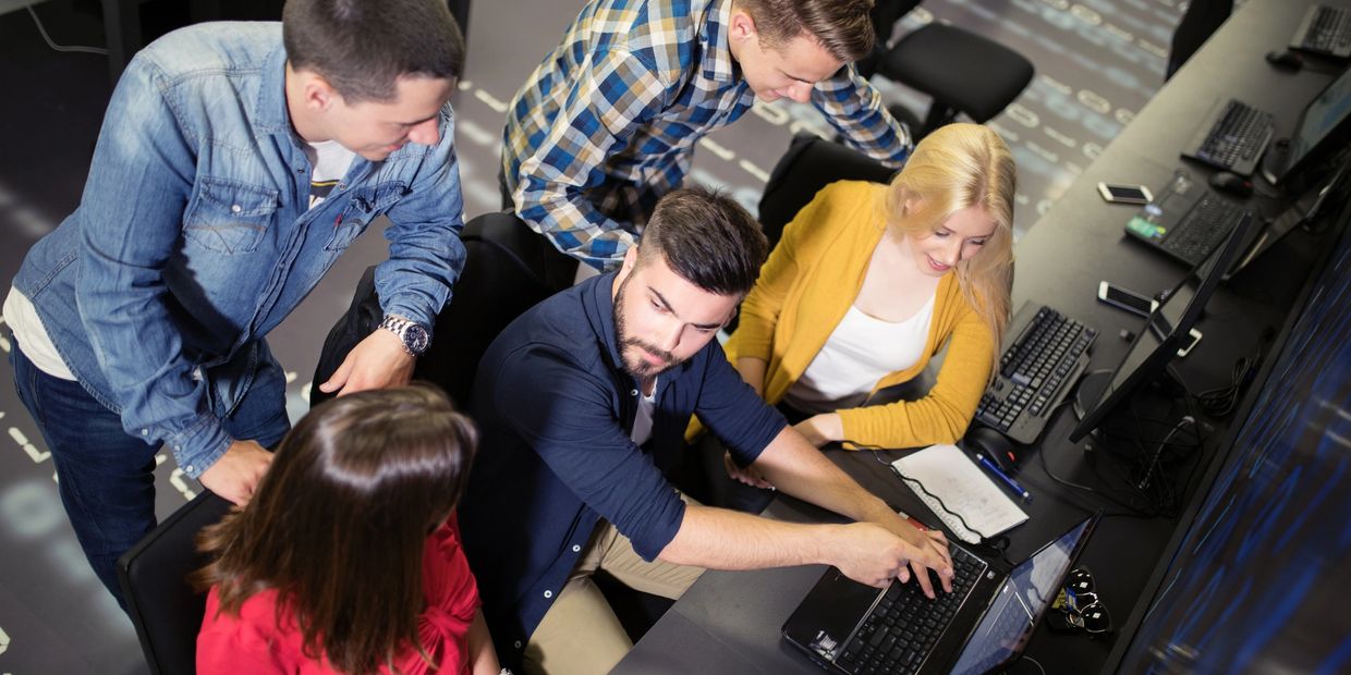Group of colleagues collaborating around a laptop in an office.