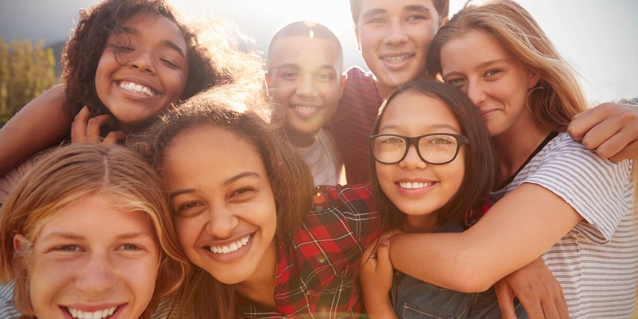 A diverse group of happy teenagers smiling closely together outdoors.