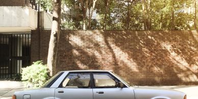 Classic white sedan parked on the street under tree shadows.