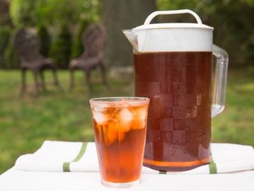 Glass and pitcher of iced tea on a table outdoors.