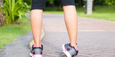 Person walking on a paved path wearing black pants and gray-pink sneakers.
