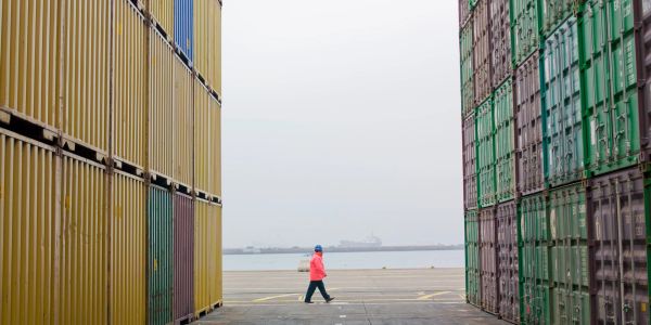 Person walking between stacked shipping containers near the waterfront.