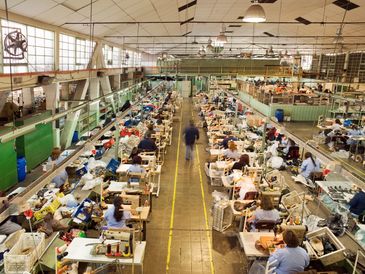 Fábrica com várias pessoas trabalhando em linhas de produção.