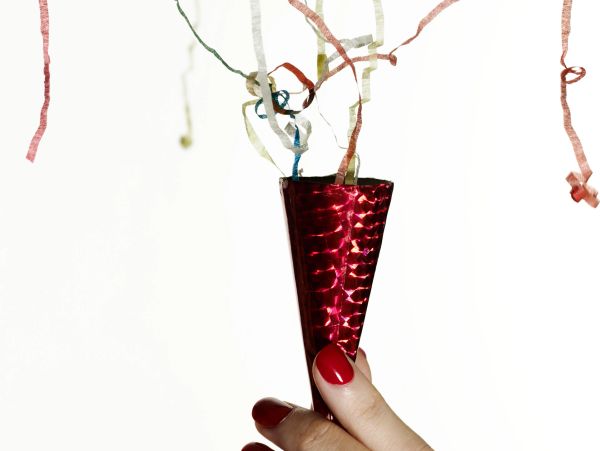 Hand holding a shiny red party popper with colorful streamers.
