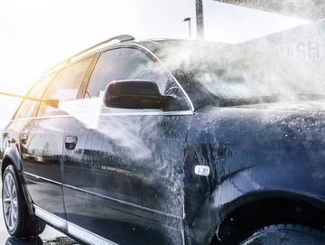 Black car being washed with a high-pressure water hose.