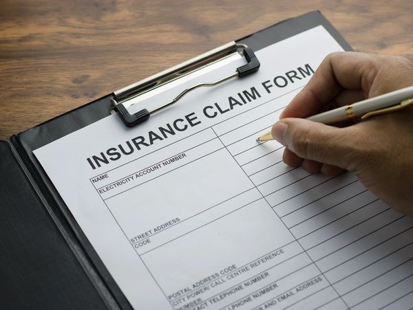 Person filling out an insurance claim form on a clipboard with a pen