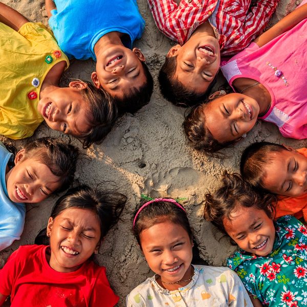 Joyful children lying in a circle on sand, smiling brightly.
