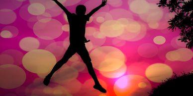 Person jumping joyfully against a colorful sunset.