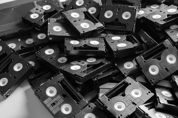 A pile of black VHS-C video cassette tapes scattered on a flat surface.