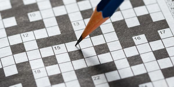 A pencil poised over a crossword puzzle grid.