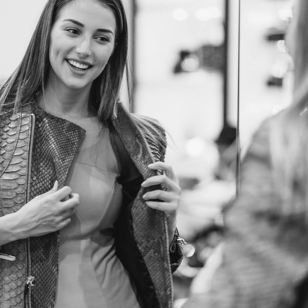 A woman smiling while trying on a blue jacket in front of a mirror.