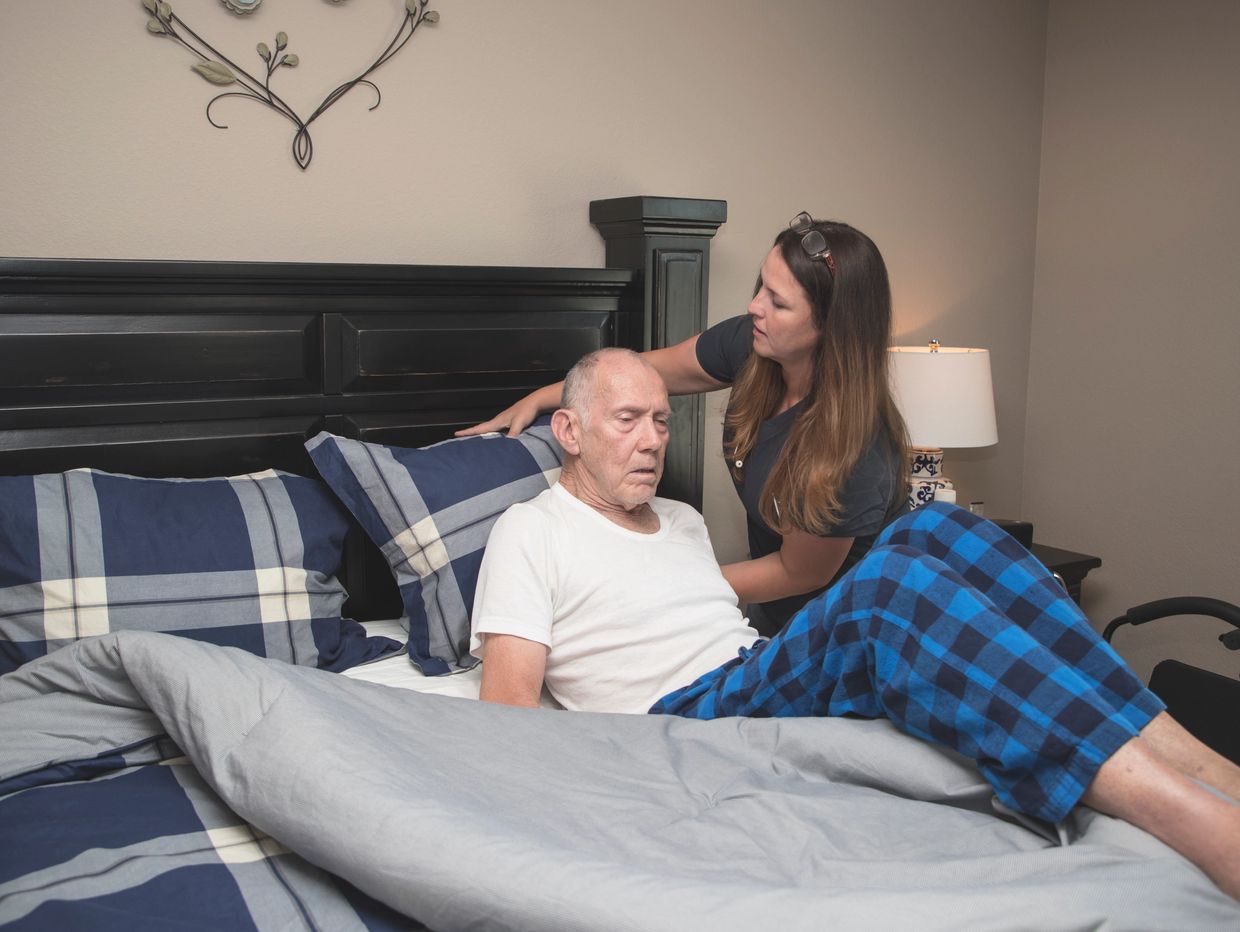A woman helping an elderly man sit up in bed.