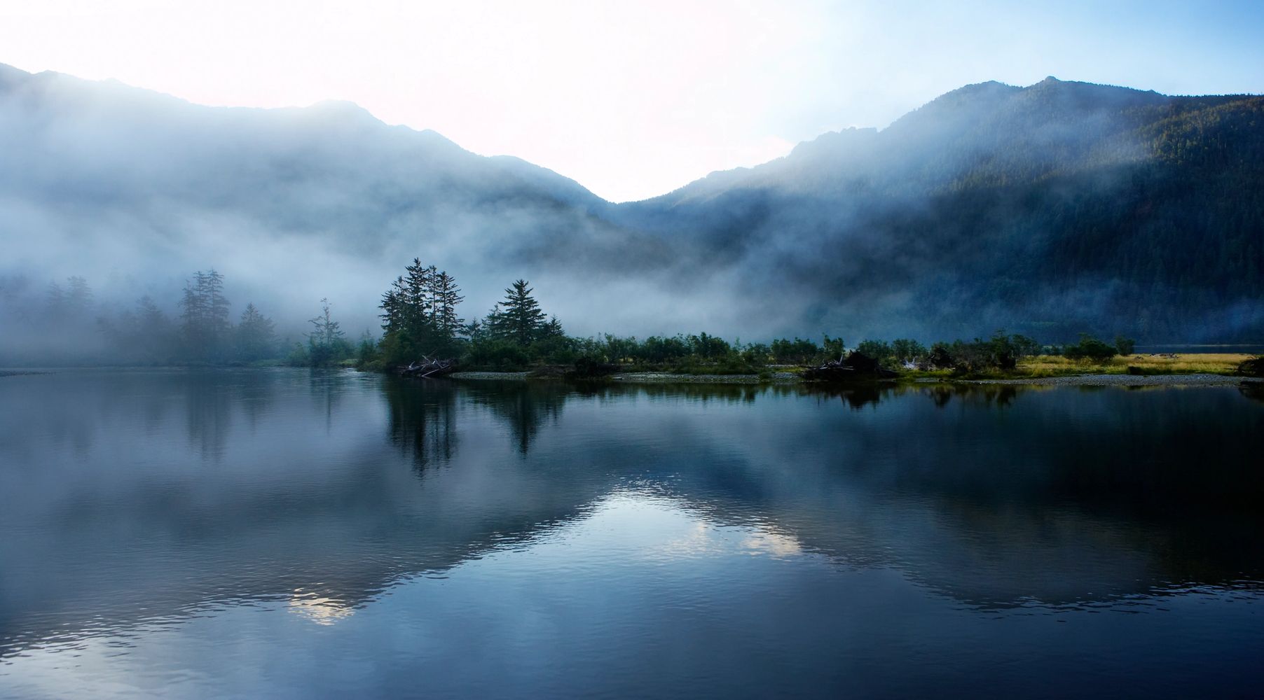 Misty mountains reflected in a calm lake at dawn.
