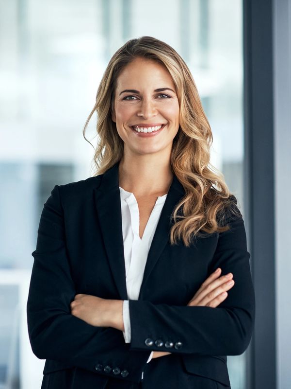 Confident businesswoman in a black suit smiling with arms crossed.
