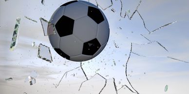 A soccer ball breaking through shattered glass against a blue sky.