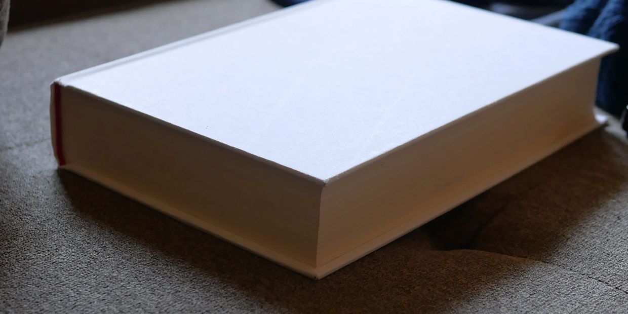 A closed thick hardcover book lying on a gray fabric surface.