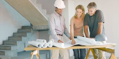 Three people reviewing building plans on a table.