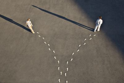 Two people walking in opposite directions with diverging footprints on the ground.