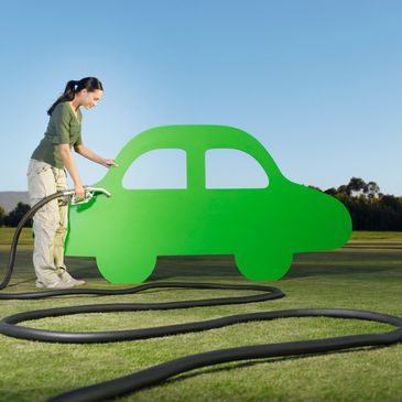Woman fueling a green car-shaped cutout with a gas nozzle outdoors.