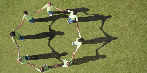 Children holding hands in a circle on grass with shadows.